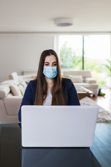 Young business woman working from home on laptop and wearing protective mask. Coronavirus quarantine concept.