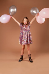 A smiling girl with an armful of balloons is dressed in a party dress.