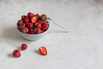 Fresh ripe tasty strawberries in a ceramic bowl on a light background. Nearby lies a dessert fork with strawberries. Top view.
