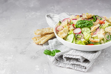 Delicious Fattoush or Arab salad with pita bread, fresh vegetables and basil on white plate. Middle...