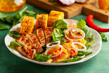  Grilled chicken breasts cooked on a BBQ served with citrus salad and corn on a plate. Close up view. Concept homemade summer dinner