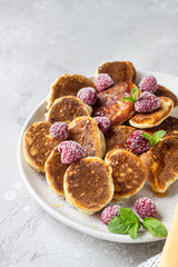 Mini pancakes with raspberries, mint and jam for breakfast on a ceramic plate. Pancakes cooked in the morning for breakfast in the home kitchen.