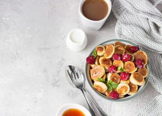 Bowl with tiny pancake cereal with raspberries, mint and jam on a light grey concrete background. Trendy food. Mini cereal pancakes. Pancake porridge.