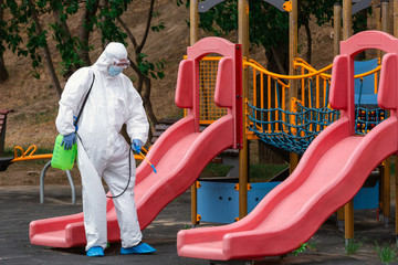 Children playground disinfecting and sanitizing against virus and disease. Man in white protective...