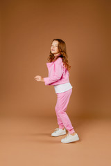 Fototapeta na wymiar cute girl in a pink tracksuit does gymnastics and does exercises on a beige background