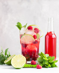 Lemonade or non-alcohol cocktail with raspberry, lime and mint in glass on grey stone background. Summer berry drink.
