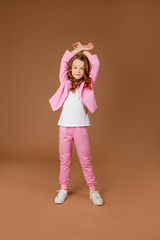 cute girl in a pink tracksuit does gymnastics and does exercises on a beige background