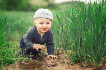 A Caucasian infant climbs in a muddy puddle.