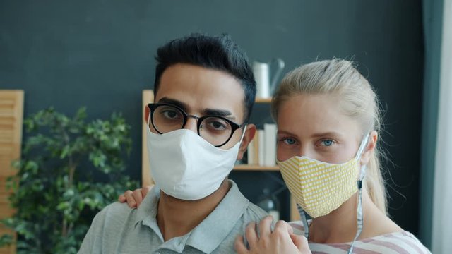 Slow motion portrait of Middle Eastern man and Caucasian woman in medical masks indoors at home during corona virus pandemic. People and lockdown concept.