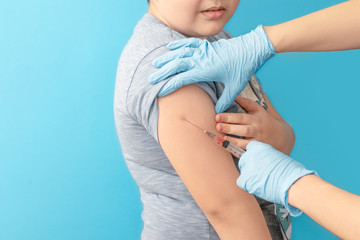 Doctor makes vaccine to child in clinic. Blue background, copy space.