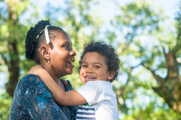 African mom happily hugging her child in nature. Great copy space.