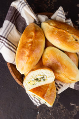Traditional Russian pies with green onion and egg on wooden plate, dark rustic background. Russian pirozhki, homemade baked patties.