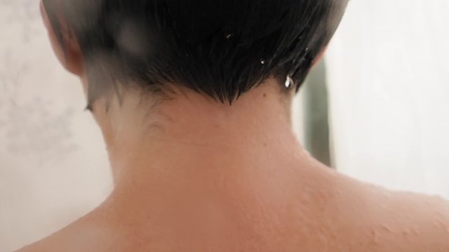 Naked woman takes a shower. Woman washes her short hair with water. Slow motion video in white bathroom.
