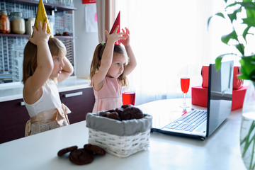 Kids virtual birthday party.Girls in dresses and caps celebrate holiday with friends on isolation.Online conference,video call in laptop,computer.Animator,juice,cookies.Quarantine,coronavirus covid-19
