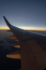 Fototapeta premium Aircraft wing silhouette seen through window in sunset sky with colorful clouds