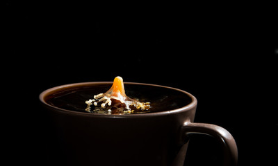 Milk droplet hitting the surface of hot coffee isolate over black background