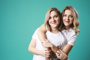 Two blonde young caucasian women twins hugging each other  in white t-shirt isolated on green background