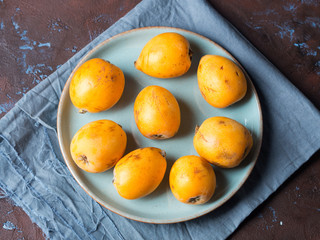 Loquat Japanese medlar fruit on blue dish on dark background. Top view