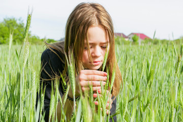 A young girl looks at a spikelet in a sown field
