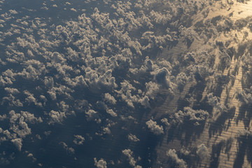 Fluffy clouds above the rippled ocean with sun reflection seen from an aircraft