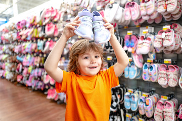 Kid in supermarket shoes shop. Sale, consumerism and people concept. Kids shoes store in supermarket, choosing kids in shoes store. Shoes store for kids.