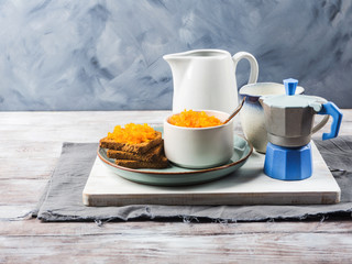 Home made carrot jam made with orange and lemon juice. Healthy vegetable jam for breakfast served in a bowl and with toasted bread on gray and blue background