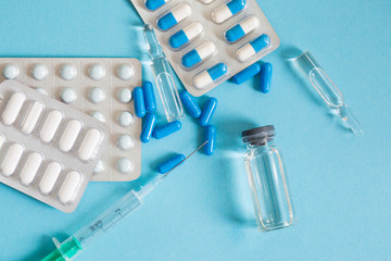 Different types of medication, tablets, capsules, ampoules and syringes on blue background.