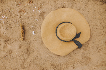 Fototapeta na wymiar Modern straw hat with seashell and dry herb on sand top view. Summer vacation concept. Summer travel accessory on real beach.