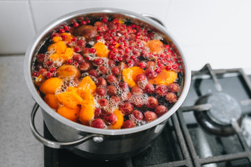 Fresh fruits are boiled in boiling water in a metal pan on the stove. Delicious stewed apricot, apples, cherries, raspberries. Photography, concept.