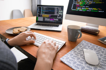 Close-up of unrecognizable programmer sitting at desk with coffee and cookies and creating code for...