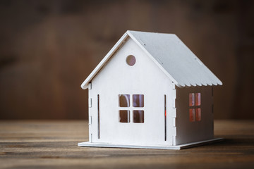 White model of a house with triangle roof on a brown wooden background.