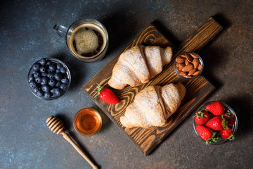 Fototapeta na wymiar Breakfast with fresh croissants, coffee and berries on dark table background