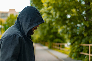 bearded man in hoodie profile portrait in the street green foliage bokeh background scenic view criminal incognito person