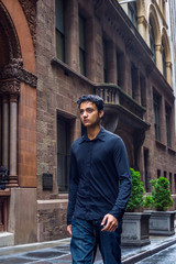 Raining day - wet, drizzle, grainy feel. Lonely East Indian American teenager wearing black long sleeve shirt,  broken fashionable jeans, walking on narrow old street in Manhattan of New York City..
