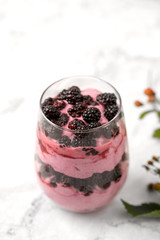 Blackberry dessert made of fresh blackberries and whipped cream in a clear glass on a white background