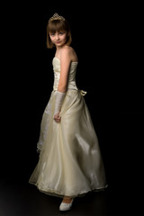 Fototapeta na wymiar A little girl in a long, elegant dress of a princess on a black background.