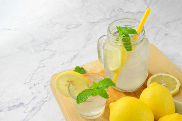 Freshly squeezed lemon juice and mint leave in clear glass cup on wooden chopping board and clean white marble background. Healthy Fruit juices that are high in vitamin C.
