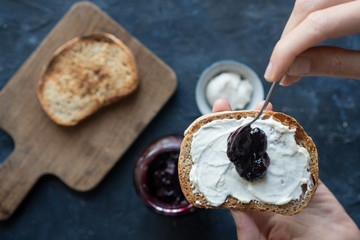 woman hand spreading raspberry jam in a sourdough bread toast with cream cheese