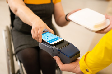 Close-up of unrecognizable woman in wheelchair taking food order and paying for lunch delivery using smartphone