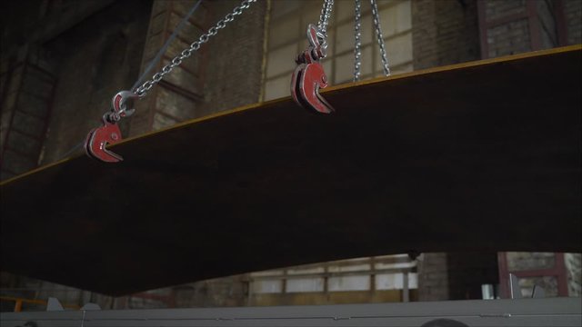 Low angle view of manual worker operating crane lifting sheet metal in industry. Crane in the factory lifts metal sheets