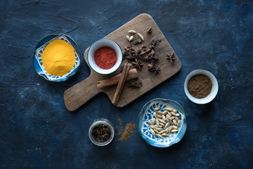 Spices for an indian tea chai infusion. Turmeric, chili, cardamom, cinnamon, cloves on a wood table and a blue background