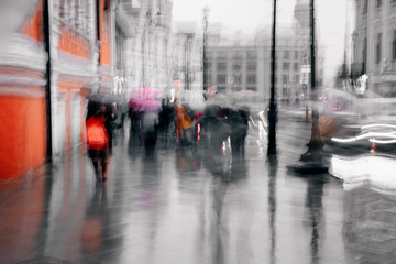Rainy cold evening in the city. Unrecognizable silhouettes of people under umbrellas walking along the street, city life. Abstract blurred background