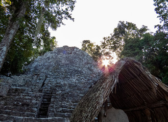 Ancient Mayan ruins with the light of a rising sun passing through the tropical trees of Coba.