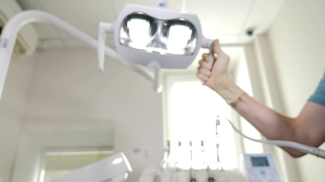 Pov dentist. Young male Friendly dentist in Mask holding mouth mirror and hook, turning Light of dental Lamp on, starting treatment. Oral hygiene and dental cure in dentistry. Stomatologist in modern