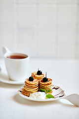 Mini-pancakes, Tiny pancakes, trendy food.
Fritters with fruit: blackcurrant, strawberry, mint. Breakfast with tea