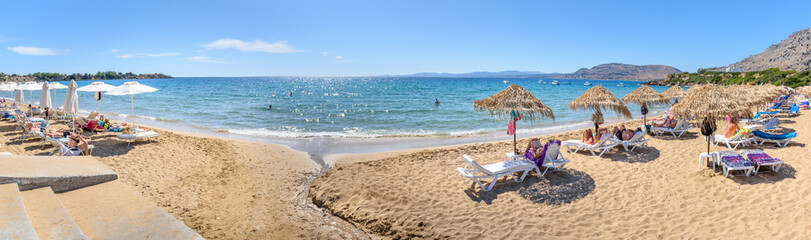 Pefkos beach with holiday-makers, sun beds and umbrellas in village of Pefkos - PANORAMA (Rhodes,...