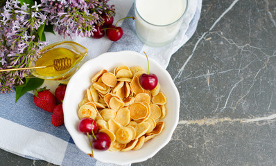 Tiny pancake cereal, cherry, strawberry, honey and milk on dark rustic background with lilac flowers