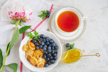 Tiny pancake cereal with blueberry, honey and tea for breakfast in the morning light and pink peony on table