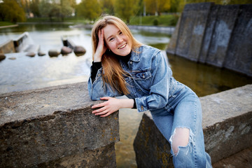 Beautiful portrait of a 90s redhead scandinavian teenager girl in jeans in a park near a lake