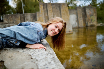 90s redhead scandinavian teenage girl in jeans plays in a park with lake water